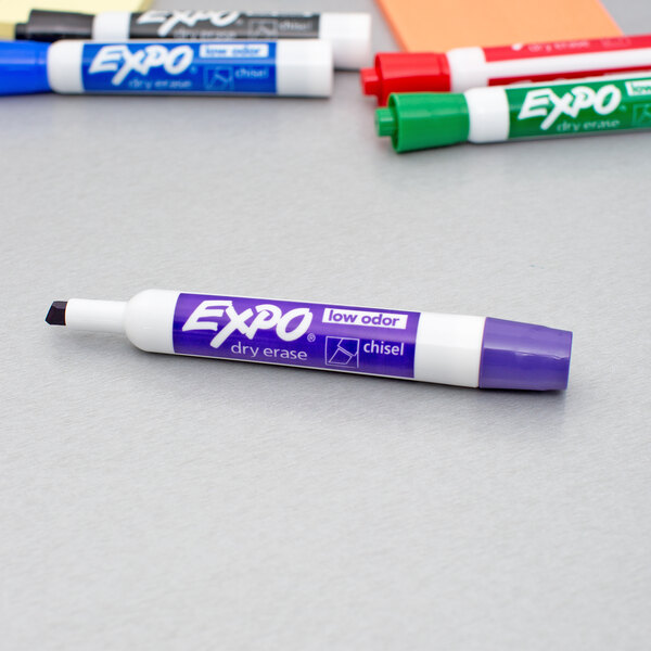 A group of colorful Expo dry erase markers in green, red, purple, blue, and black with white caps.