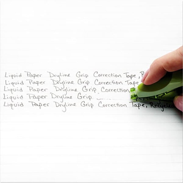 A hand using Paper Mate Liquid Paper Correction Tape to cover green writing on paper.
