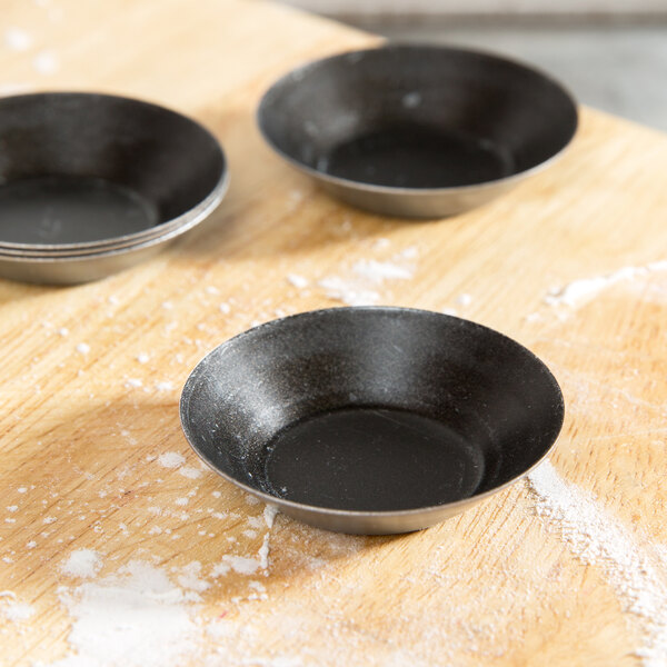 A black Matfer Bourgeat tartlet pan on a wood surface.