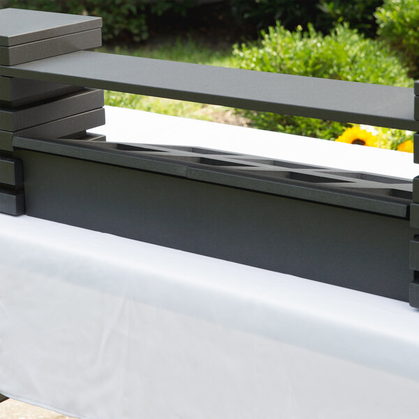 A black rectangular Vollrath wood crossbar on a white table outdoors.