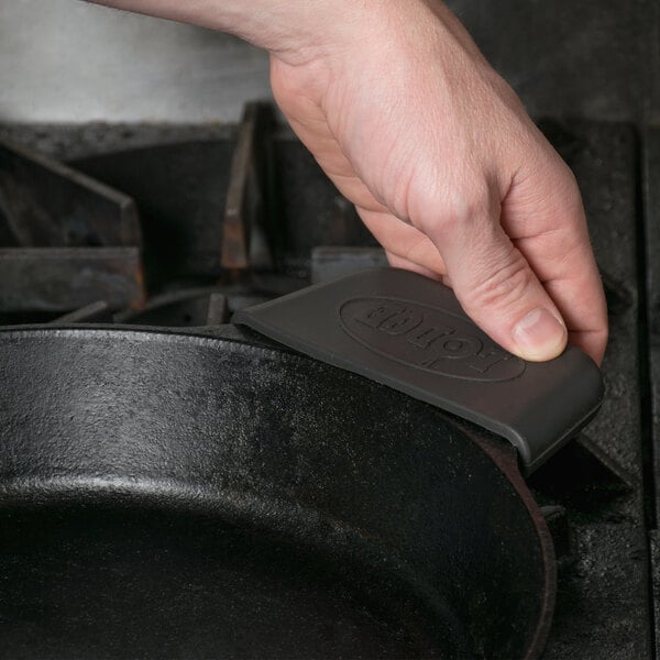 A person's hand using a Lodge black silicone handle holder to hold a pan.