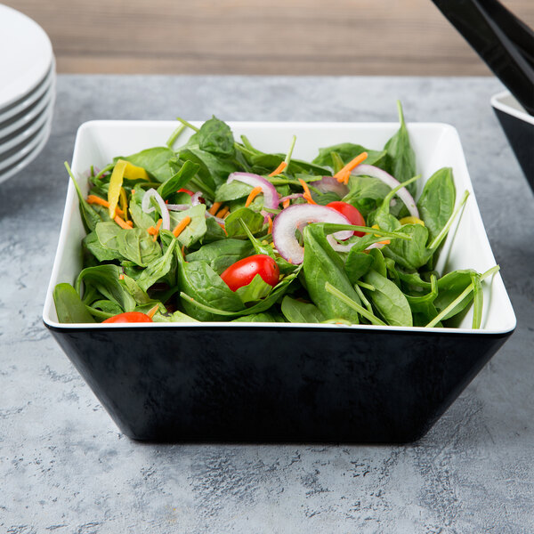 A bowl of salad with tomatoes and onions in a black melamine bowl.