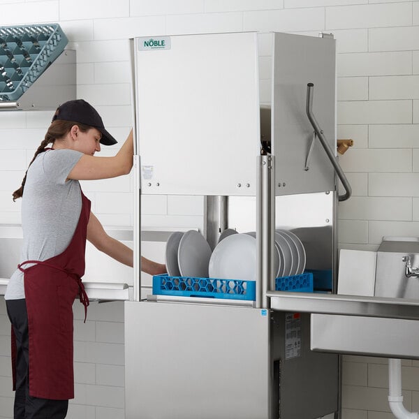A commercial high temperature dishwasher with a person loading dishes into it.