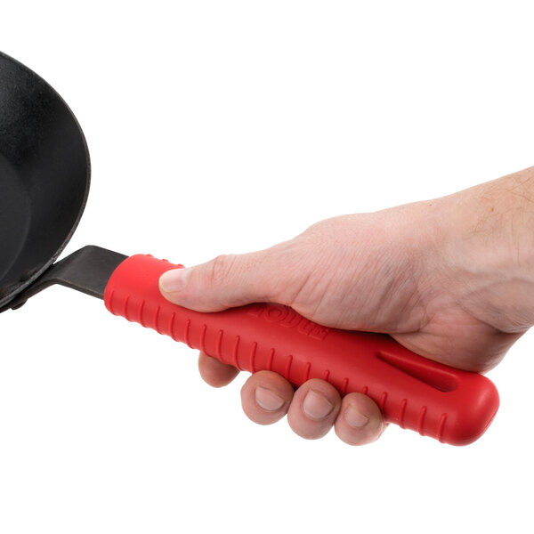 A hand holding a red Lodge silicone handle holder over a black skillet.