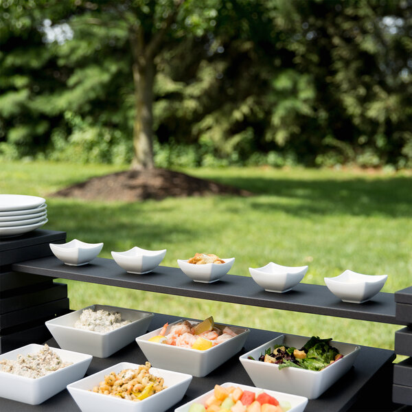 A group of white bowls of food on a black wood narrow shelf.