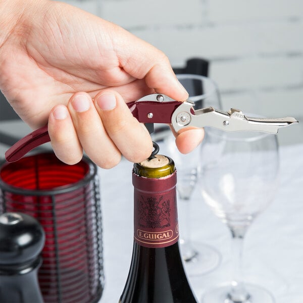 A hand using a red Pullparrot Waiter's Corkscrew to open a wine bottle.