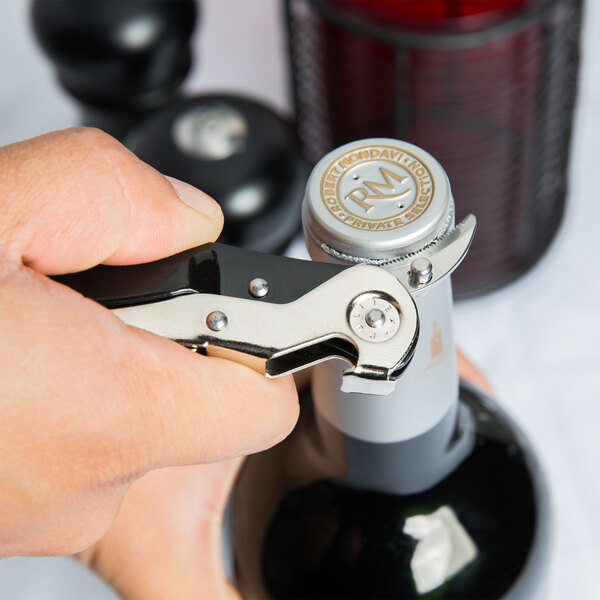 A person using a Pullparrot waiter's corkscrew with a black and silver knife to open a bottle of wine.