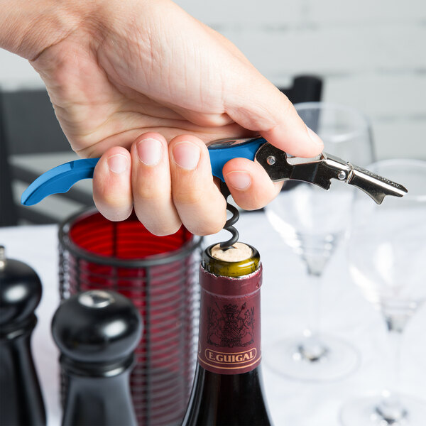 A hand holding a Pulltap's Original Waiter's Corkscrew with Electric Blue handle opening a bottle of wine.