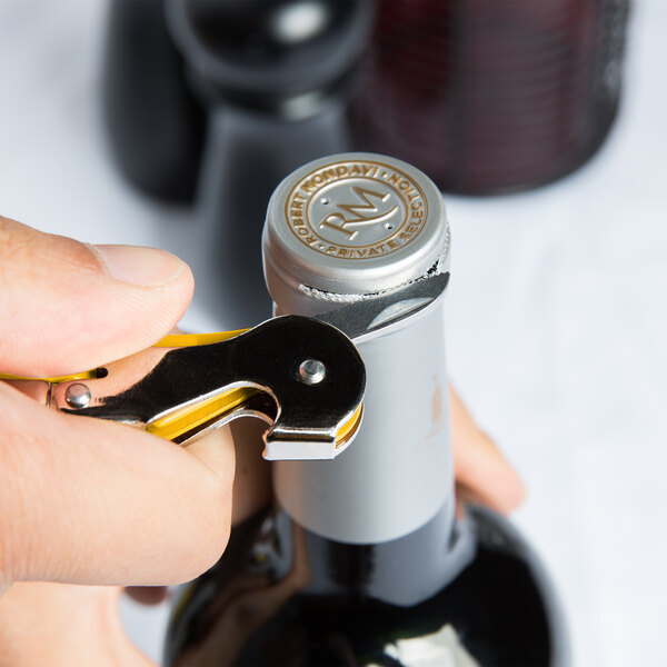 A hand using a yellow Pulltap's Original corkscrew to open a bottle of wine.