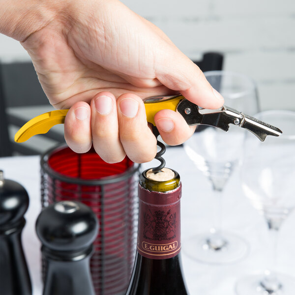 A hand using a yellow Pulltap's Original corkscrew to open a bottle of wine.