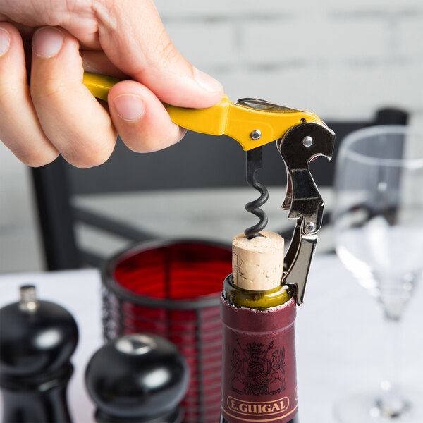 A hand holding a Pulltap's Original Waiter's Corkscrew with a yellow handle opening a bottle of wine.