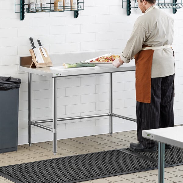 A man in an apron standing at a Regency stainless steel work table.