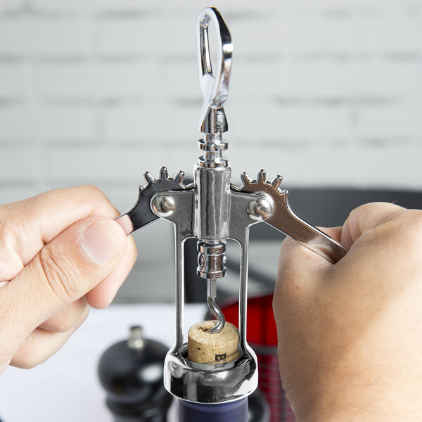 A person using a Franmara Tavern wing corkscrew with a chrome body to open a bottle of wine.