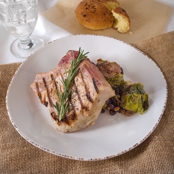 A white irregular melamine bowl with a piece of meat and vegetables in it on a table.