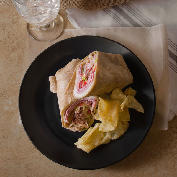 A black matte round melamine plate with a sandwich and chips on it.