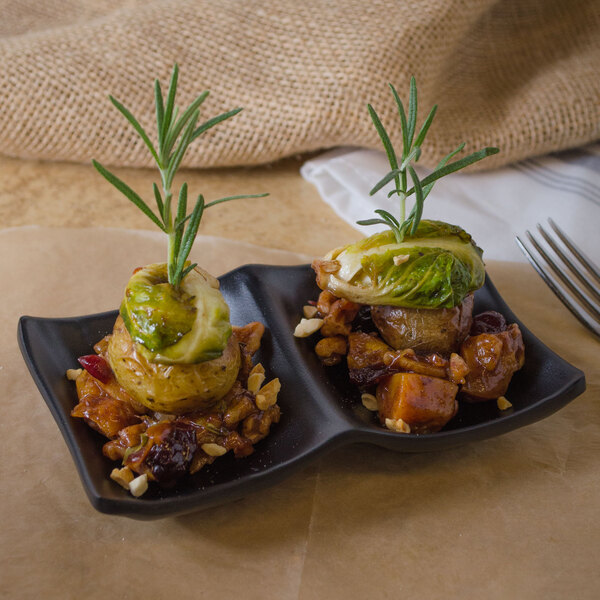 Two black matte melamine sauce dishes with food on them and a sprig of rosemary.