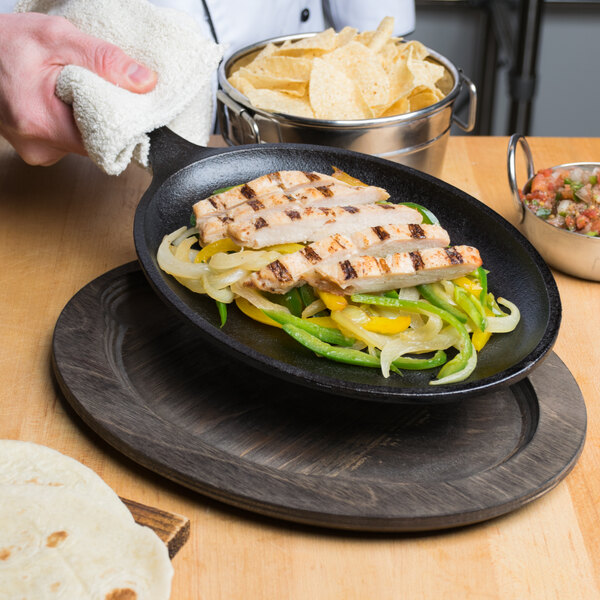 A person using a Lodge cast iron fajita skillet to prepare food on a table.