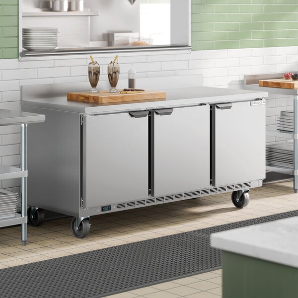 A stainless steel three-door worktop refrigerator with a 4-inch foamed-in-place backsplash on casters.