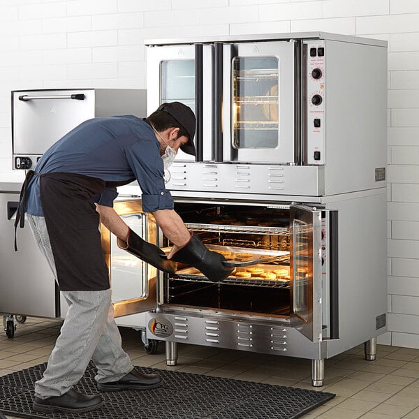 A man wearing a black apron putting food into a Cooking Performance Group double deck convection oven.