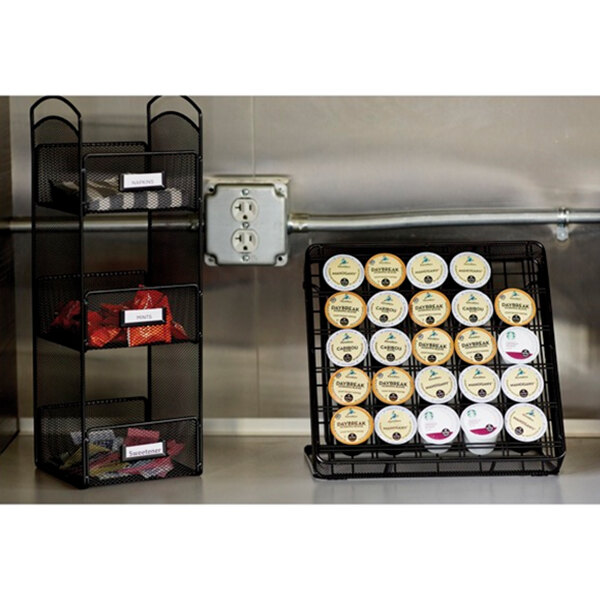A Safco black wire mesh organizer on a counter with coffee pods and red packets.