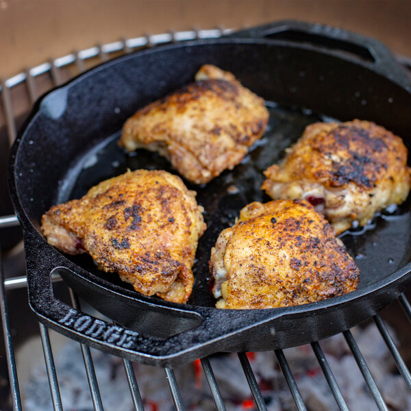 A Lodge cast iron skillet with three chicken legs cooking in it.