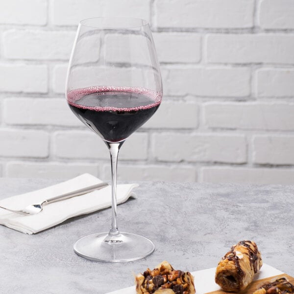 A close-up of a Spiegelau burgundy wine glass filled with red wine next to chocolate and nuts.