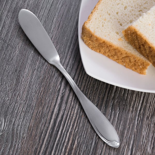 A plate with a slice of bread and a Oneida Scroll stainless steel butter knife.