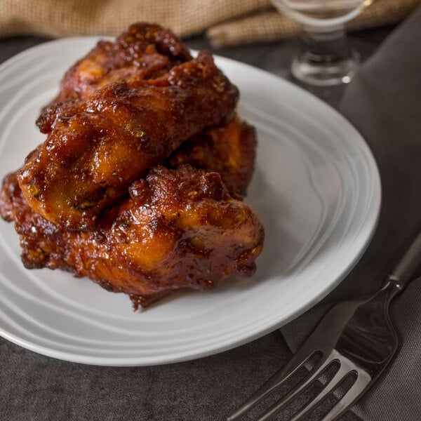 A GET Magnolia ivory melamine oval coupe platter with a textured rim holding chicken wings.