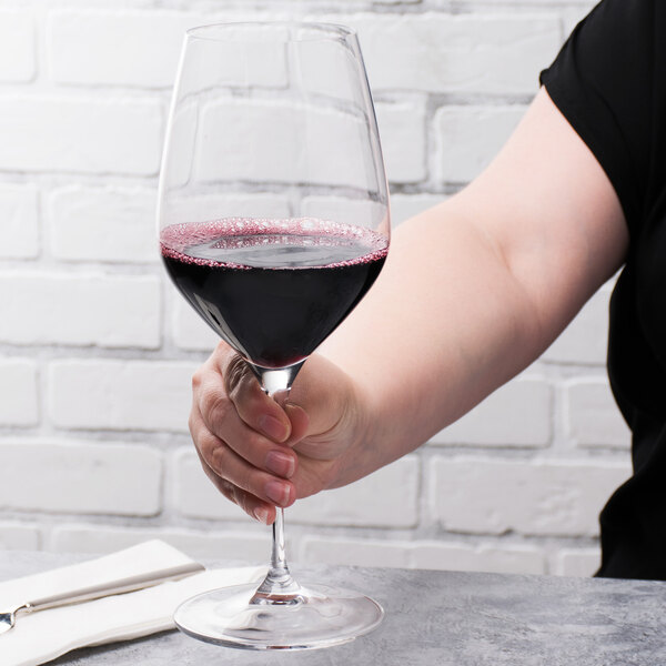 A hand holding a Spiegelau Bordeaux wine glass full of red wine.