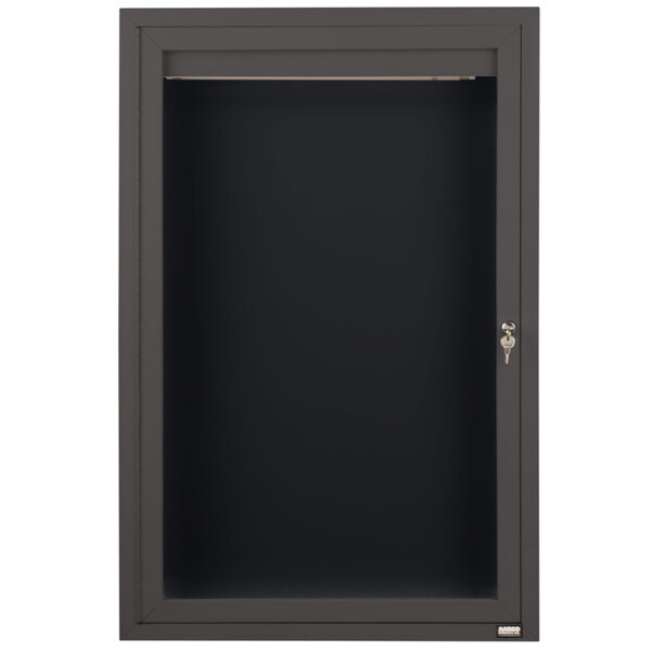 A black metal cabinet with a key and a glass door with a black letter board inside.