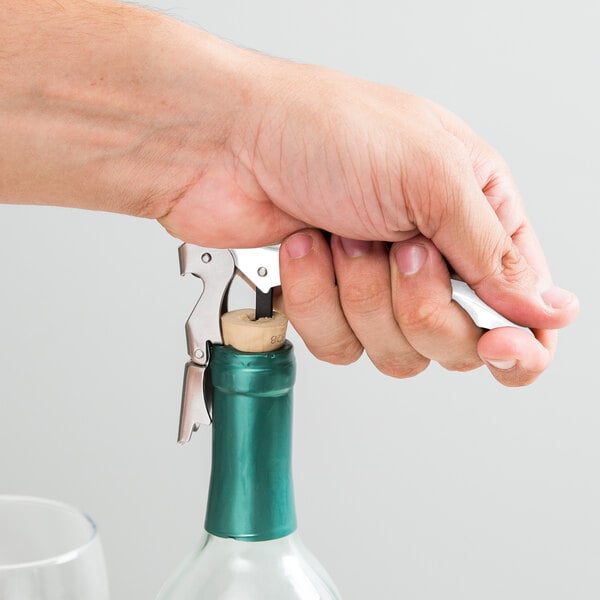 A hand uses a Franmara Duo-Lever corkscrew with a white enamel handle to open a bottle of wine.