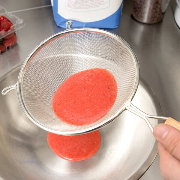 A Tablecraft fine tin single mesh strainer holding a red substance over a bowl.