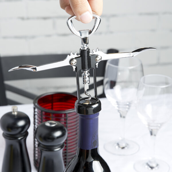 Hand holding top of wing corkscrew and twisting it into wine cork