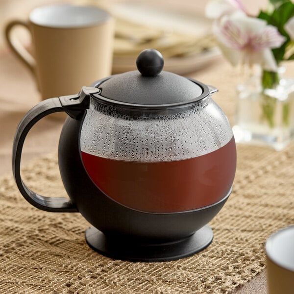 A round tempered glass tea pot infuser with a black handle and lid, filled with tea.