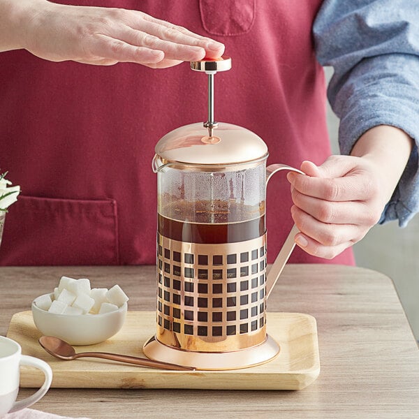 A person using an Acopa Glass / Copper French Coffee Press to press coffee on a counter.