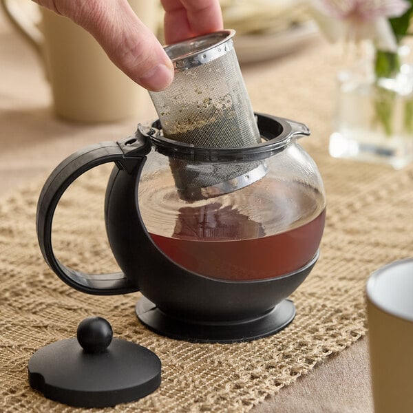 A 25 oz. tempered glass tea pot infuser with a black handle and base, shown with a stainless steel basket being removed.