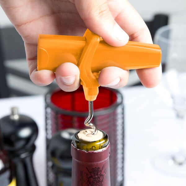 A hand using a Franmara Traveler's Orange plastic corkscrew and bottle opener to open a wine bottle.