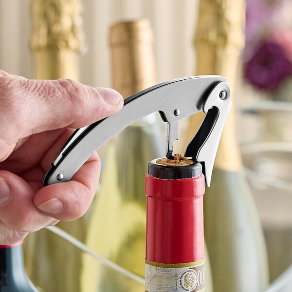 A hand using a Franmara curved stainless steel waiter's corkscrew to open a wine bottle.