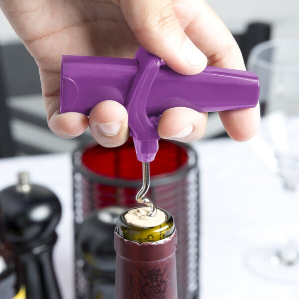 Hand holding purple pocket corkscrew and using it to remove cork from wine bottle