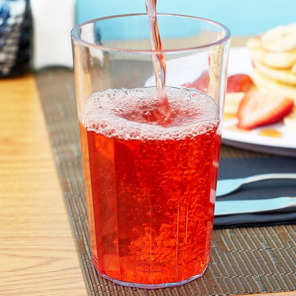 A person's hand pouring red liquid into a Cambro Newport plastic tumbler.