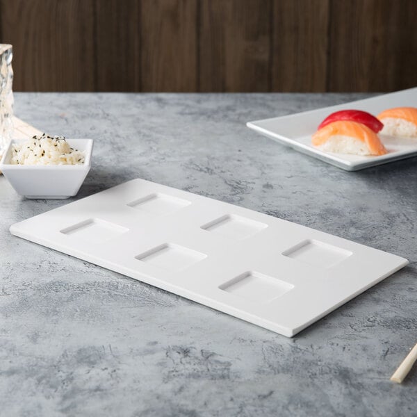 A white rectangular melamine tray with square cutouts holding sushi.