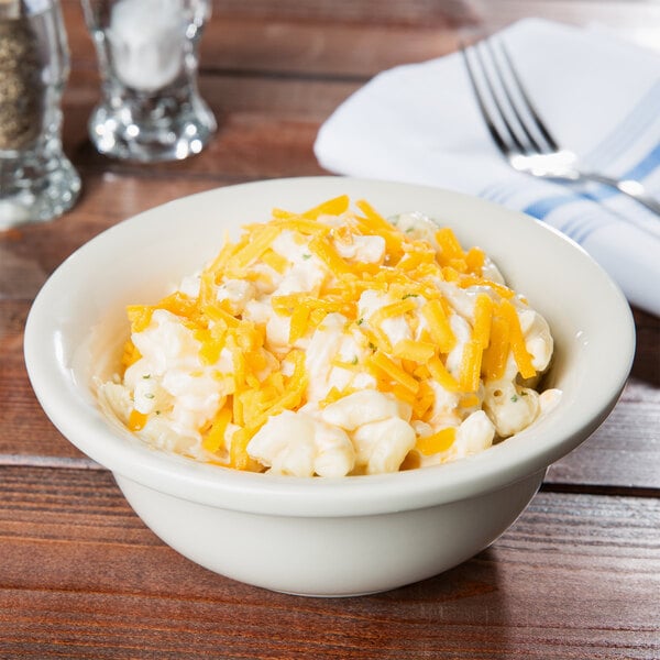 A Hall China ivory pot pie baking bowl filled with macaroni and cheese on a table with a fork and knife.