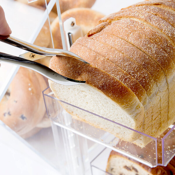 A person cutting a loaf of bread on a table in a bakery display.