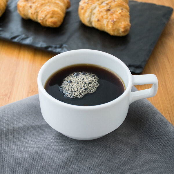 A Libbey alpine white porcelain stacking cup filled with coffee on a table with croissants.