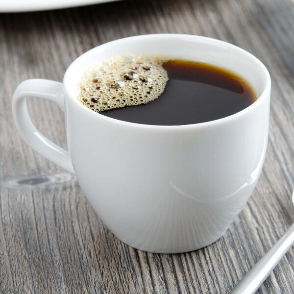 A white Libbey porcelain cup filled with brown coffee on a wooden table.