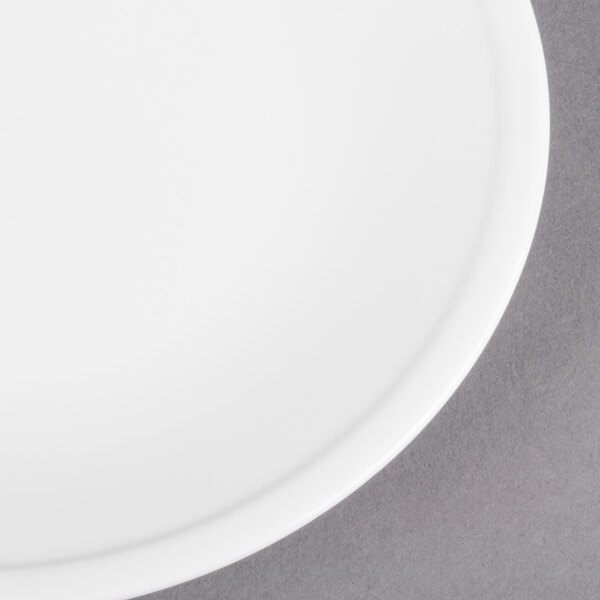A Libbey Alpine White Porcelain Coupe Plate with a white rim on a gray surface.