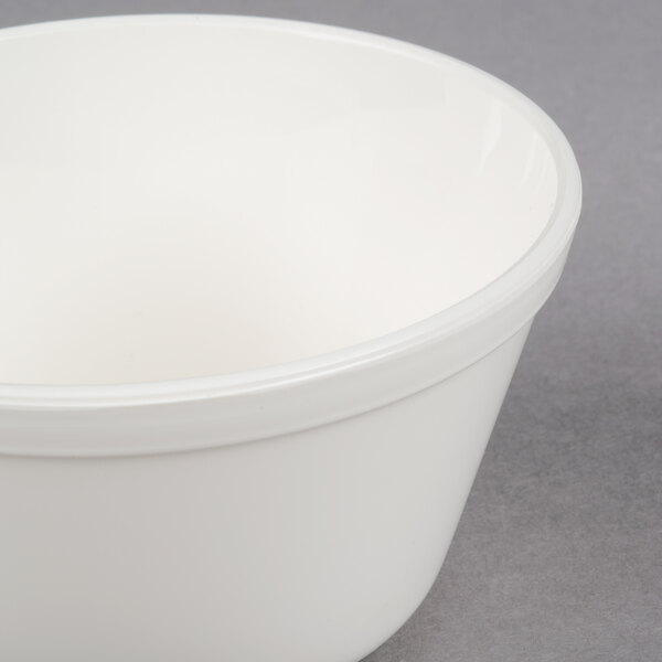 A close up of a white Carlisle polycarbonate bouillon cup on a gray surface.