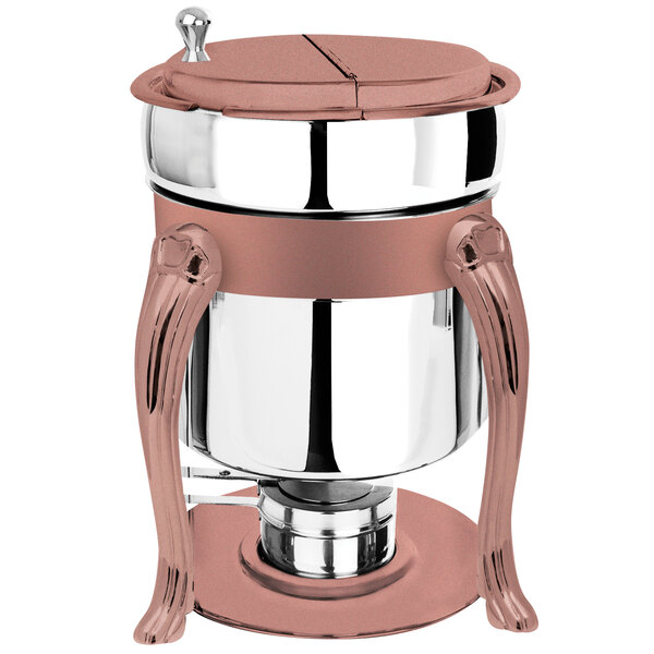 A stainless steel soup marmite with copper accents on a table with a fuel holder.