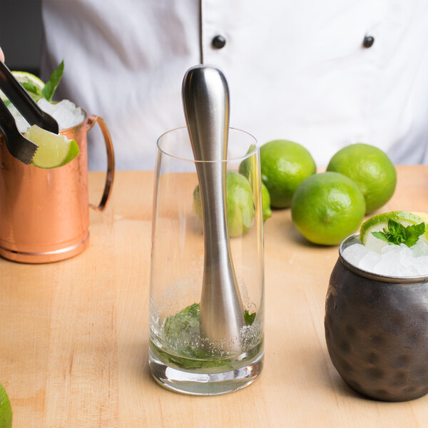 A person using a Franmara stainless steel muddler with a metal head to muddle a lime in a glass.