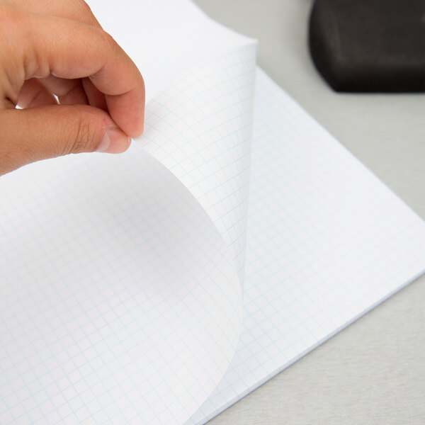 A hand holding a TOPS quadrille ruled writing pad with a pen.